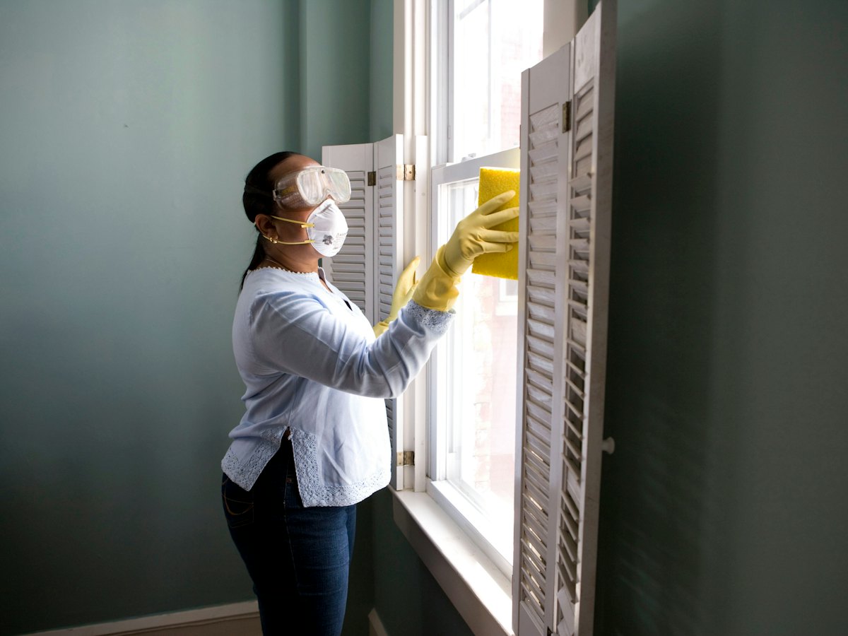 A cleaner in gloves wiping down a window frame